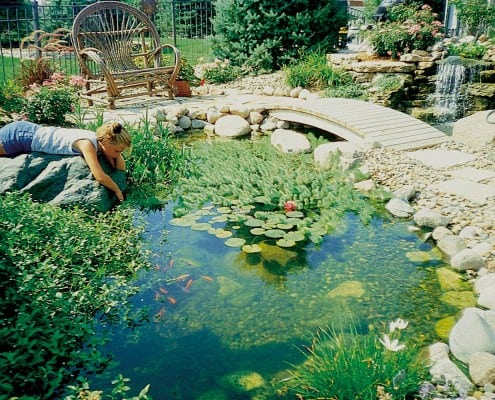 Koi pond with young girl sitting with arm reaching into water