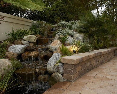 Stone water fall into pond next to paving stone wall
